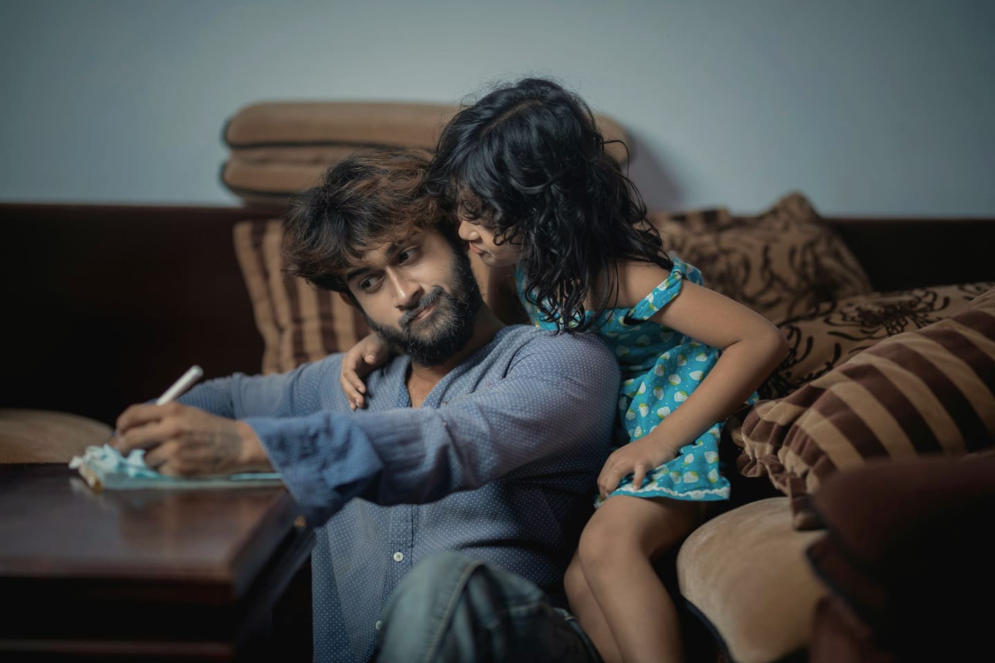 A father writing while his daughter leans in to watch